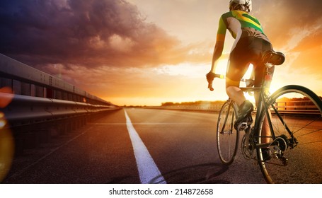 Cyclist riding a bike on an open road to the sunset 