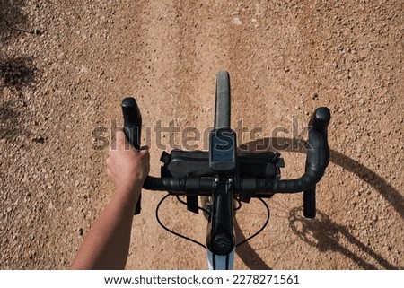 Cyclist riding a gravel bike on a gravel path while holding the handlebar's top grip.Cyclist is shown holding the top grip of a gravel bike handlebar, riding on a gravel path in the mountains.Alicante