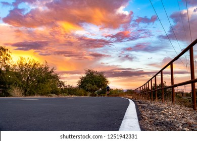 A Cyclist Riding Their Bicycle Under A Colorful Sky At Sunset On The Loop A Paved Biking, Running, Jogging And Walking Path That Is In Pima County, Tucson, Arizona. Pink, Lavender, Blue Green Colors.