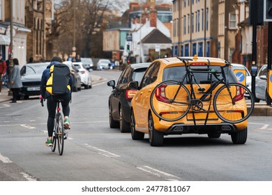 Cyclist riding through city streets with a backpack, alongside cars, one carrying a bike on the rear rack. Ideal for illustrating urban commuting, city traffic, eco-friendly transportation urban life - Powered by Shutterstock