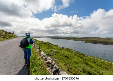 Cyclist stopping on the Sky Road coastal road admiring the spectacular scenery of the Connemara coastline, back to the camera, reflective vest and helmet, sunny day in Clifden, County Galway, Ireland - Powered by Shutterstock