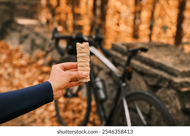 Cyclist taking a break to enjoy a delicious energy bar amidst the stunning autumnal foliage. Perfect for healthy living, sports nutrition, and outdoor adventure themes. Sports snack for cyclist. - Powered by Shutterstock