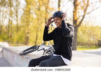 Cyclist Who Fell Off His Bike, A Bmx, And Is Sitting On A Concrete Ramp, Prepares To Get Back On Track With Friends, Puts Helmet On Head