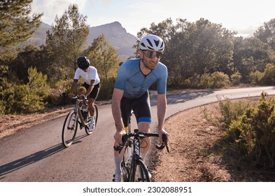 Cyclists in full cycling gear and helmets ride their road bikes on mountain road at sunset. Sportsmen training hard on bicycle outdoors. Spain - Powered by Shutterstock