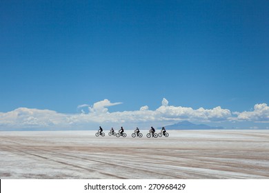 groupe de cyclistes faisant du sel dans le désert, à salares de Uyuni, en Bolivie. Nuages blancs à l'horizon, sur fond bleu ciel