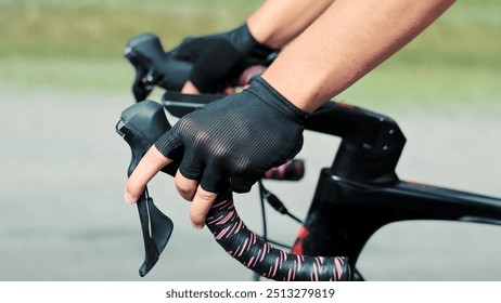 Cyclist's hands while riding a bicycle close-up side view. Cyclist wearing gloves gripping road bike handlebars. Close-up of a cyclist's hands wearing black gloves while gripping the handlebars of a - Powered by Shutterstock