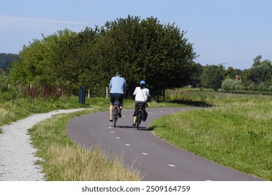 Cyclists on the cycle path (called Paddenpad) next to a shell walking path in the Dutch village of Bergen. Meadows, forest. Summer, August, Netherlands                               