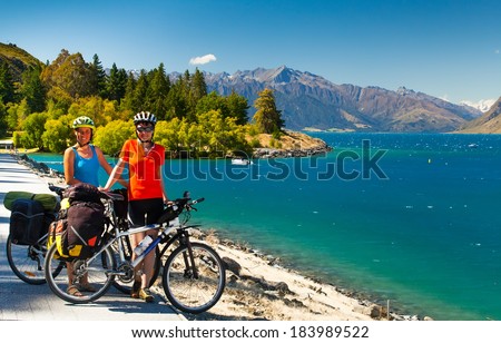 cyclists are on the winding gravel mountain road near Lake Pukaki view from Glentanner Park Centre near Mount Cook, on a background of blue sky with clouds, snowy Southern Alps.