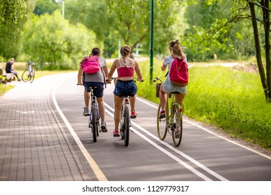 Cyclists Ride On The Bike Path In The City Park 