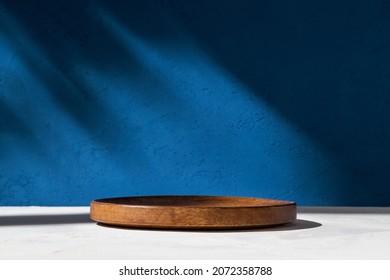 Cylinder shape wooden podium, stand and deep shadow on blue wall background. Background for product. Front view. Mockup.