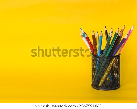 cylinder shaped metal net box pencil holder isolated on yellow background. many colored pen , education concept , copy space area. High quality photo