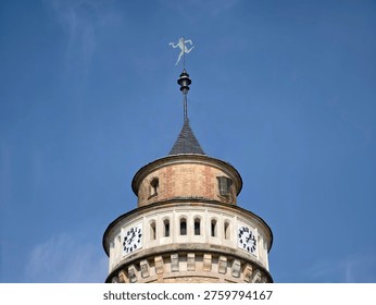 Cylindrical clock tower against clear sky, round clock openings and decorative cornice detail weathervane atop