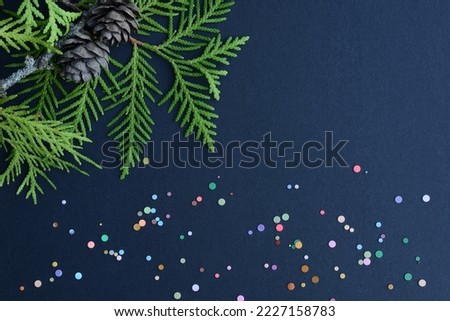 Cypress branches, pine cones and multicolor confetti on black background. Winter holiday concept. Flat lay, top view.