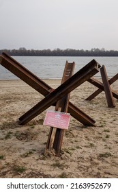 Czech anti tank hedgehogs and warning sign on river bank. Antitank obstacles on sand. Defensive war of Ukraine against Russian aggression. Inscription in different languages DANGER MINES!