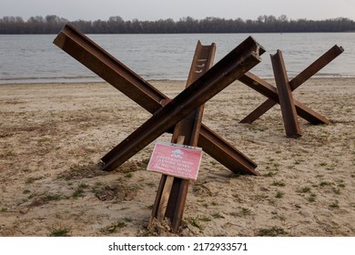Czech anti tank hedgehogs and warning sign on river bank. Antitank obstacles on sand. Defensive war of Ukraine against Russian aggression. Danger Mines! in 4 languages