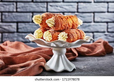 Czech kremrole: traditional pastry filled with buttercream frosting, served on a white cake stand in front of black brick wall on a dark concrete background, close-up  