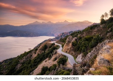 The D824 road winding its way along the coast from Capu Rossu towards Piana on the west coast of Corsica as the early  morning sun lights up the distant mountains