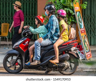 Da Nang, Vietnam - March 10, 2019: Man rides dark blue Honda Vision scooter and transports two young kid girls with him. Street scene in front of restaurant and pedestrian.