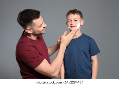 Dad applying shaving foam on son's face, grey background