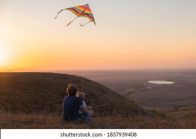 Dad And Baby Boy Fly A Kite At Sunset.