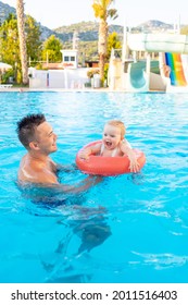 Dad And Baby In An Inflatable Circle In The Pool With Water Slides In The Summer Have Fun Swimming, Relaxing And Spending Time With The Family