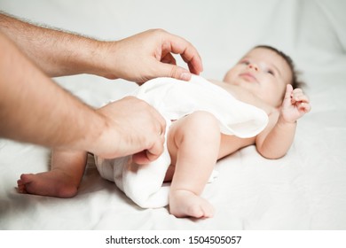 Dad Changing Baby Girl's Nappies, Infant Newborn Lying On The Bed While Daddy's Dressing Her