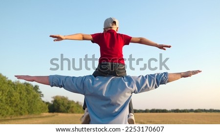 Dad, child fantasize, kid aviator sits on his fathers shoulders. Concept of happy family, childhood dream. Father Son play together in front of sun, dream, fly. Boy plays pilot airplane, hands wings