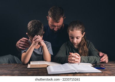 Dad and children are praying. An open Bible on the table. A group of Christians pray to Jesus. In the room - Powered by Shutterstock