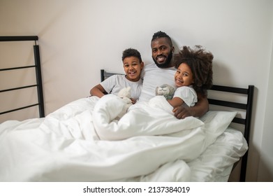 Dad With Children Reclining In Bed Looking At Camera