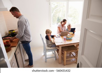 Dad Cooking And Mum With Kids At The Kitchen Table