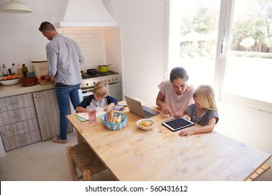 Dad Cooking And Mum With Kids At Kitchen Table, High Angle