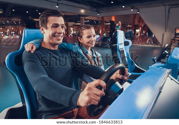 Dad\
and daughter are driving and driving game car. Little daughter\
supports dad who drives a toy car in a video game.\
