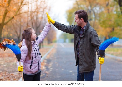 Dad And Daughter In The Park With Brooms Clap Each Other.