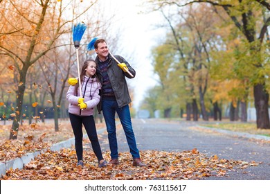 Dad With Daughter In Park With Brooms On Shoulders