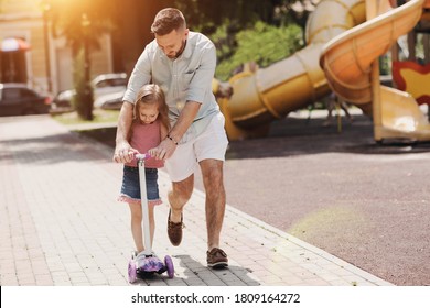 Dad with daughter in park teaching to ride scooter - Powered by Shutterstock