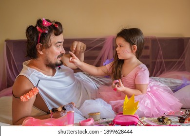 Dad And Daughter Are Playing Together. A Child Makes A Make-up For A Man. Girl In Ballet Dress Applies Sequins To Dad's Face