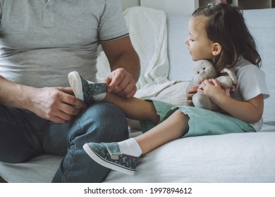 Dad and daughter sitting on couch. Father helps child to take off or put on shoes. Kid smiles - Powered by Shutterstock