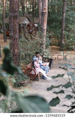 Dad and daughters are sitting on a bench in a pine forest.