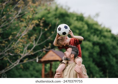 Dad having fun with young son, playing football, carrying boy on shoulders. Playing on a lawn in front of their house. Fatherhood and Father's Day. - Powered by Shutterstock