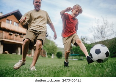 Dad having fun with young son, playing football, running and kicking the ball. Playing on a lawn in front of their house. Fatherhood and Father's Day. - Powered by Shutterstock