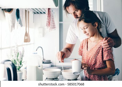 Dad With His 10 Years Old Kid Girl Cooking In The Kitchen, Casual Lifestyle Photo Series. Child Making Breakfast With Parent Together. Cozy Homely Scene.