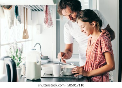 Dad With His 10 Years Old Kid Girl Cooking In The Kitchen, Casual Lifestyle Photo Series. Child Making Breakfast With Parent Together. Cozy Homely Scene.