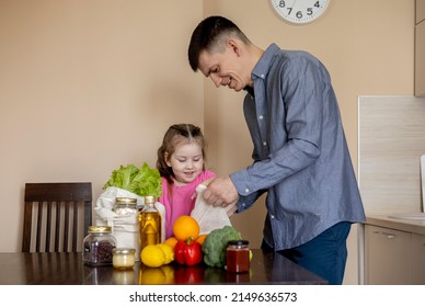 Dad and his daughter are pulling food out of the bag. Purchases from the store. Reusable package. Zero waste. Vegetarian family. Conscious consumption. - Powered by Shutterstock