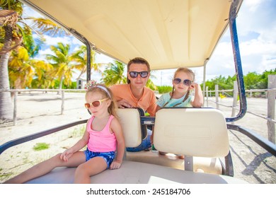 Dad and his little girls driving golf cart on tropical beach