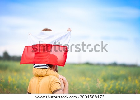 Dad with his little son on his shoulders walking in the field holding flag of Poland. Father's day in Poland. Polish Flag Day. Independence Day. Love Poland, travel concept. Selective focus.