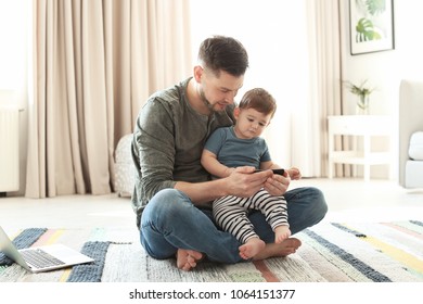 Dad And His Son With Phone On Carpet At Home