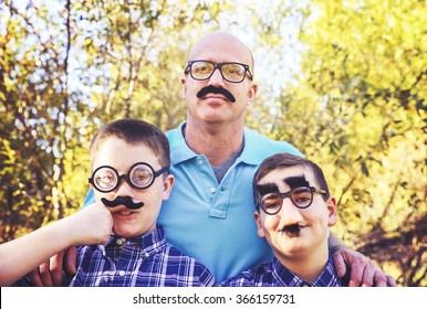 A Dad With His Sons All Acting Goofy Wearing Mustaches During A Summer Day Toned With A Retro Vintage Instagram Effect App Or Action