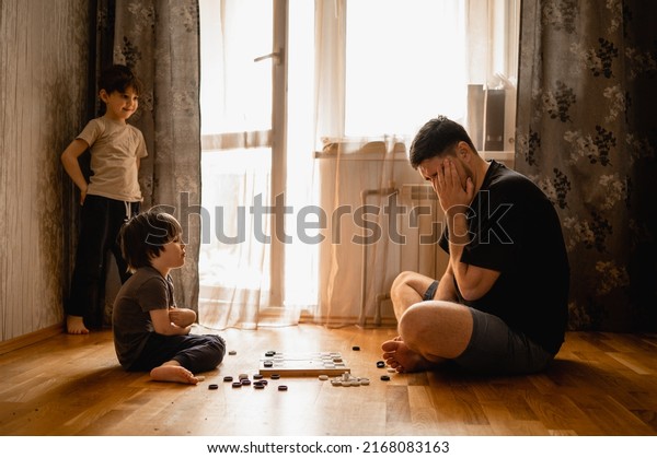 dad and his
sons play checkers. A father spends time at home after work with
his children. The concept of a large friendly family. Communication
between father and children