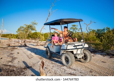 Dad with his two daughters driving golf cart at tropical beach