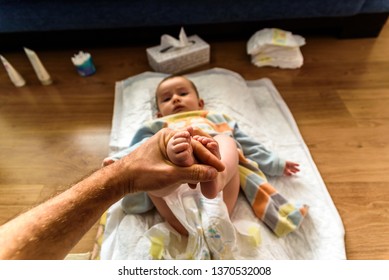 Dad Holding A Baby's Feet While Changing His Diaper.